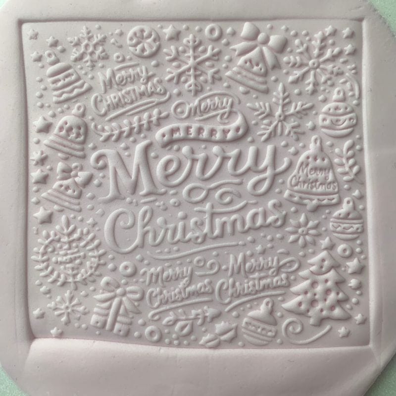 Square fondant cookie with Merry Christmas lettering and festive details using an acrylic cookie stamp